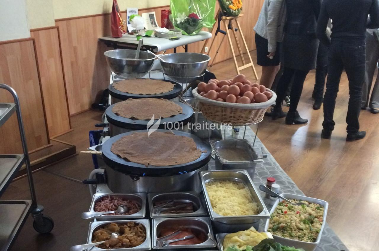 Stand de préparation de crêpes avec garnitures variées, œufs en panier et personnes en arrière-plan.