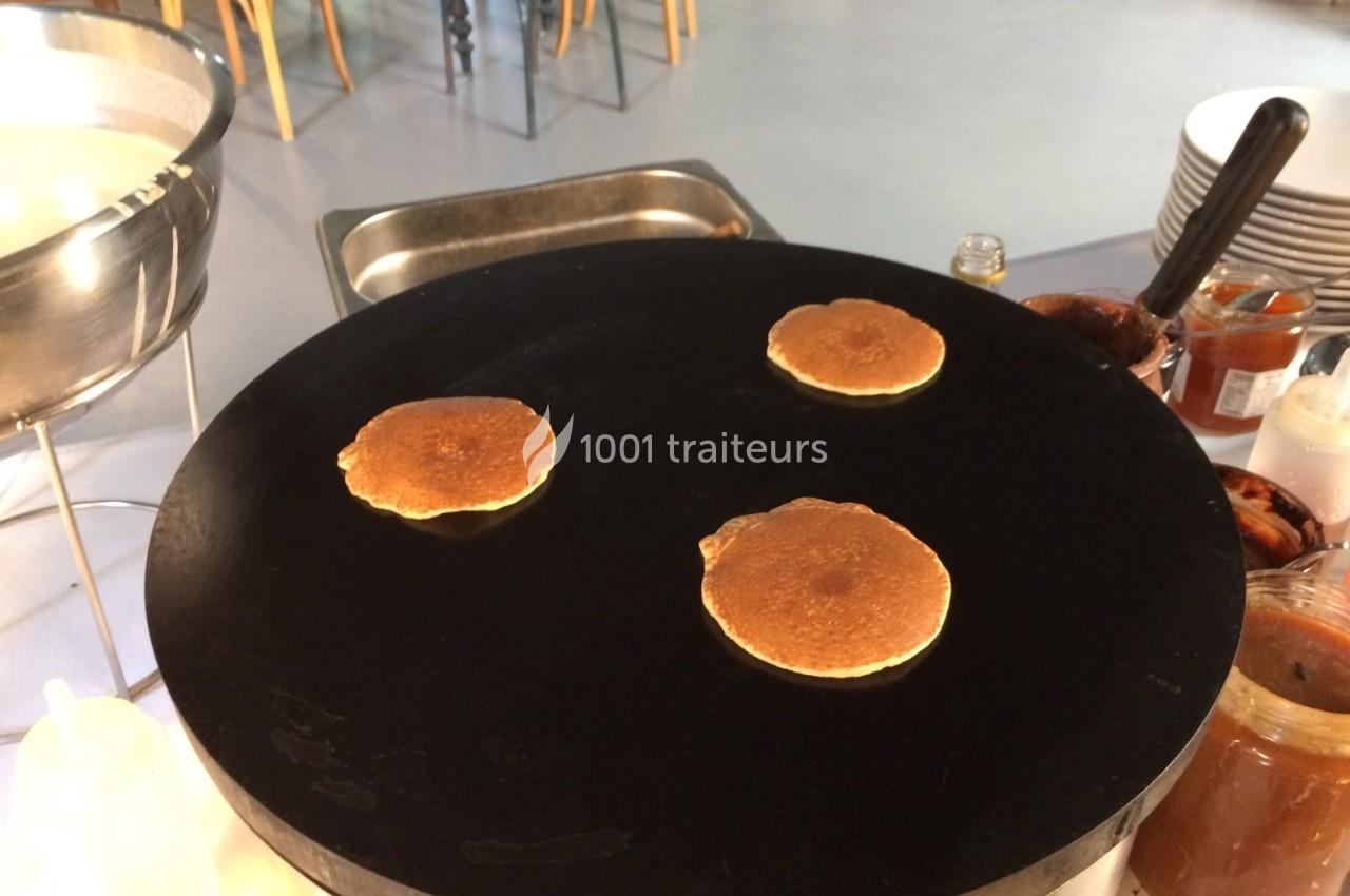 Trois pancakes cuisent sur une grande plaque chauffante noire dans un espace de cuisine.