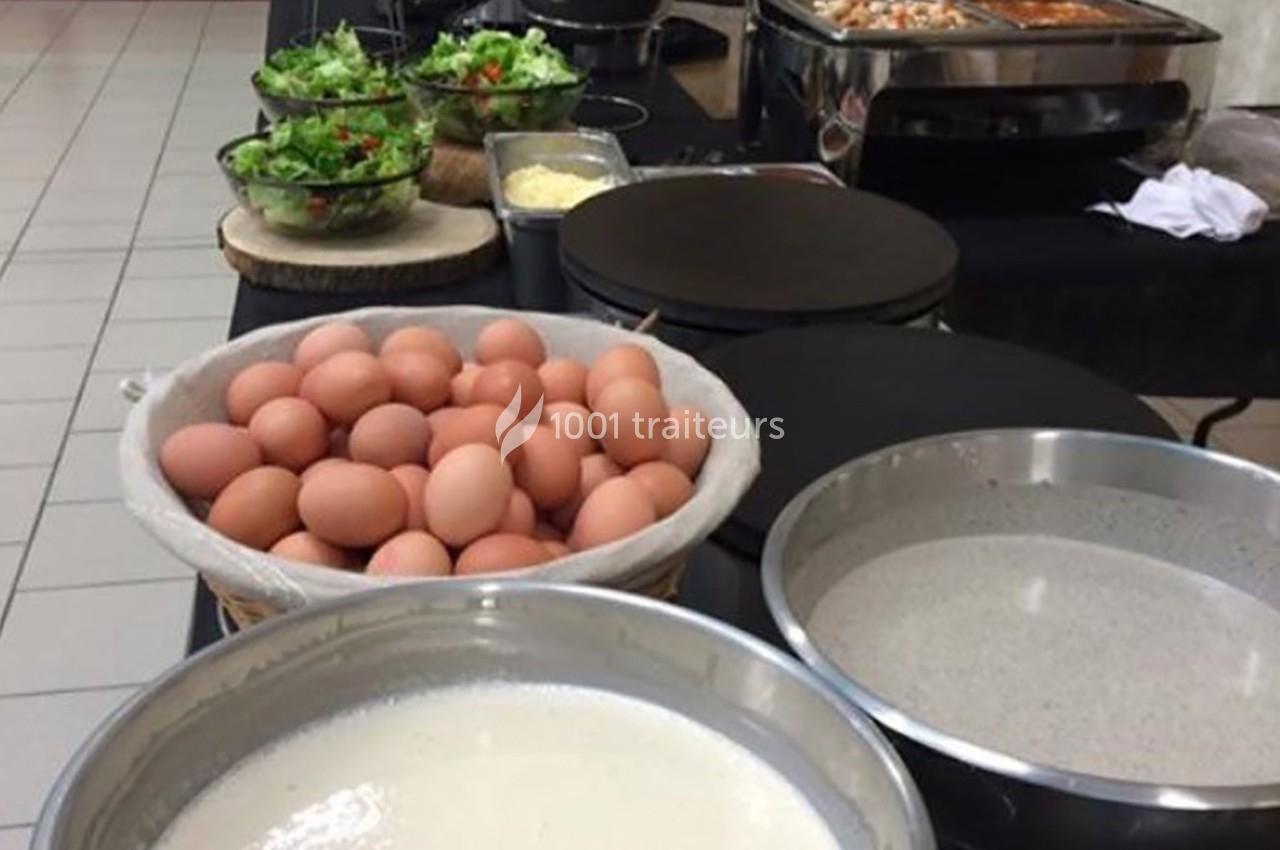 Table avec des ingrédients pour crêpes : œufs, pâte à crêpes, salades et appareils de cuisson en arrière-plan.