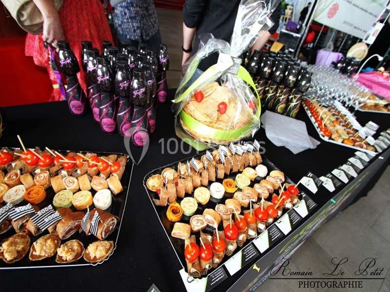 Plateaux de bouchées apéritives variées disposés sur une table avec des bouteilles et des verres en arrière-plan.
