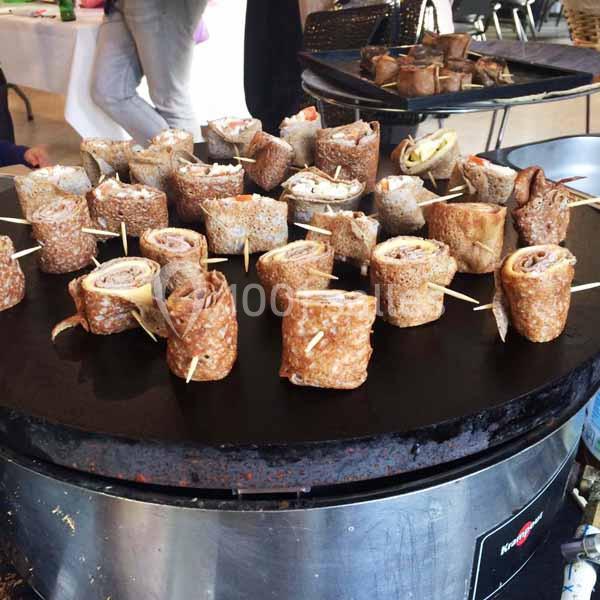 Crêpes roulées garnies, maintenues par des piques, disposées sur une grande plaque de cuisson ronde.