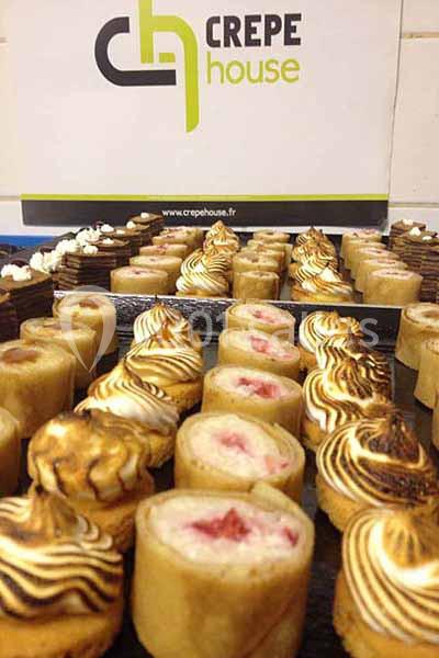 Assortiment de crêpes roulées garnies, présentées sur un plateau devant un panneau ’Crepe House’.