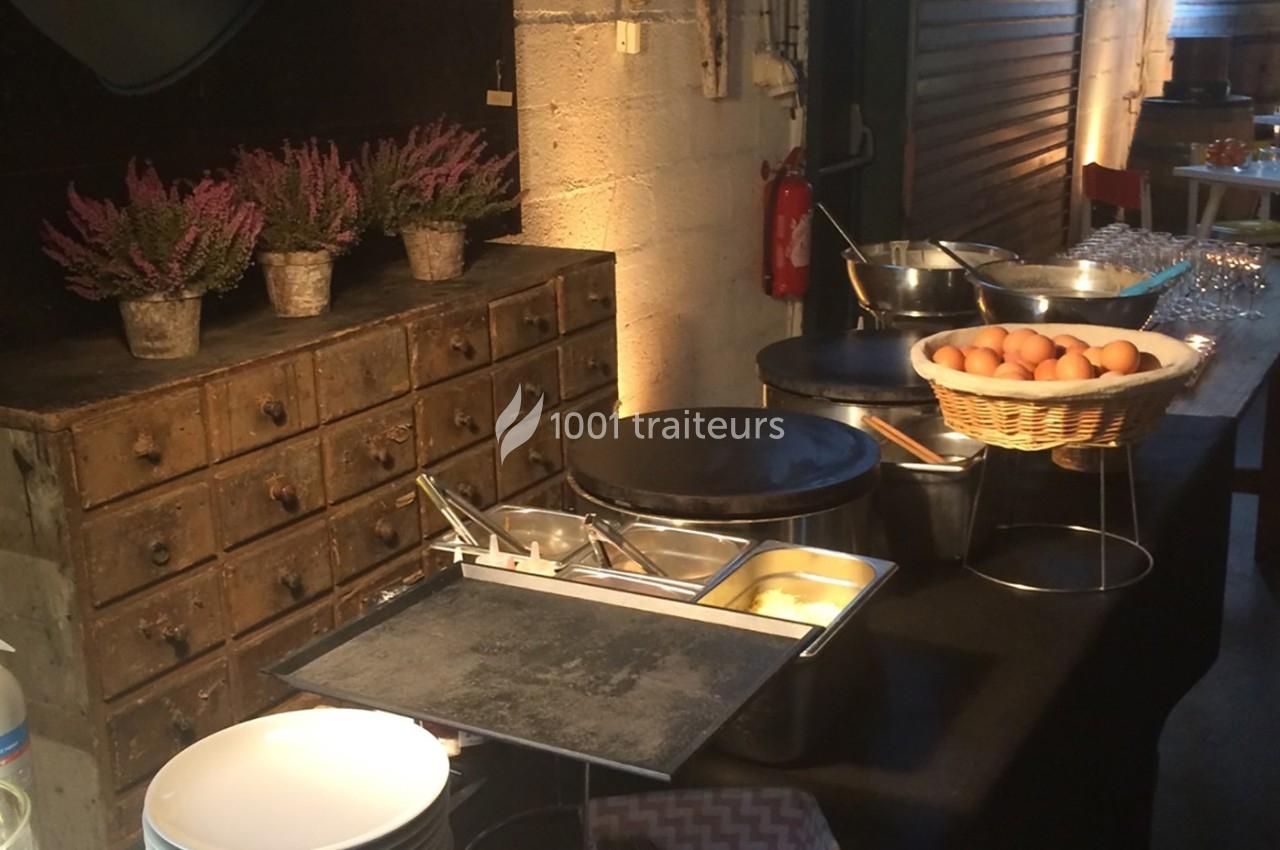 Buffet avec crêpières, bols d'ingrédients, panier d'œufs et décoration de plantes sur un meuble en bois.