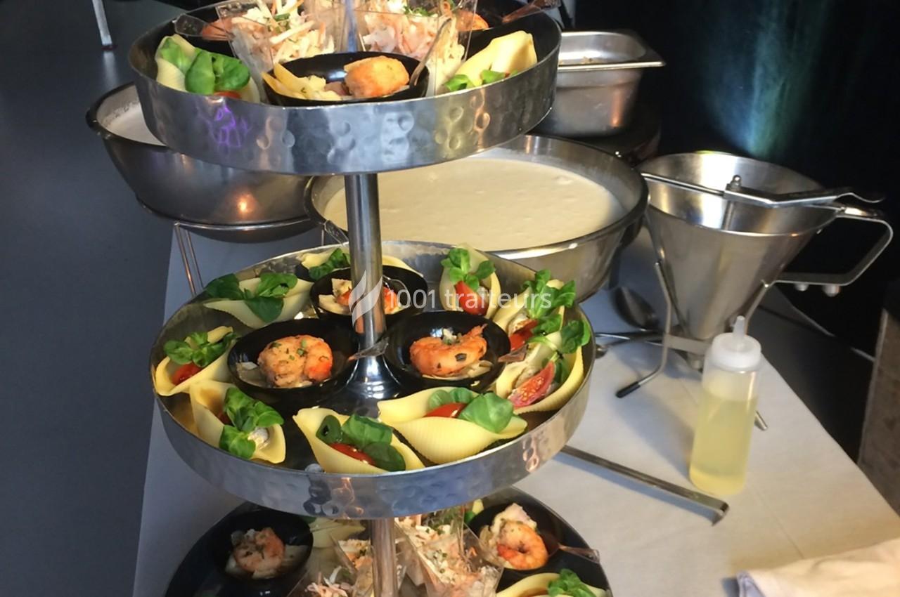 Plateau à étages avec des coquilles garnies de crevettes, légumes et herbes, présenté sur une table de buffet.