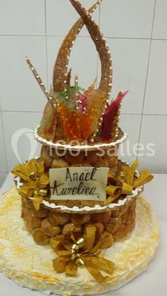 Pièce montée en choux décorée de caramel, rubans dorés et éléments en sucre coloré, sur une base blanche.