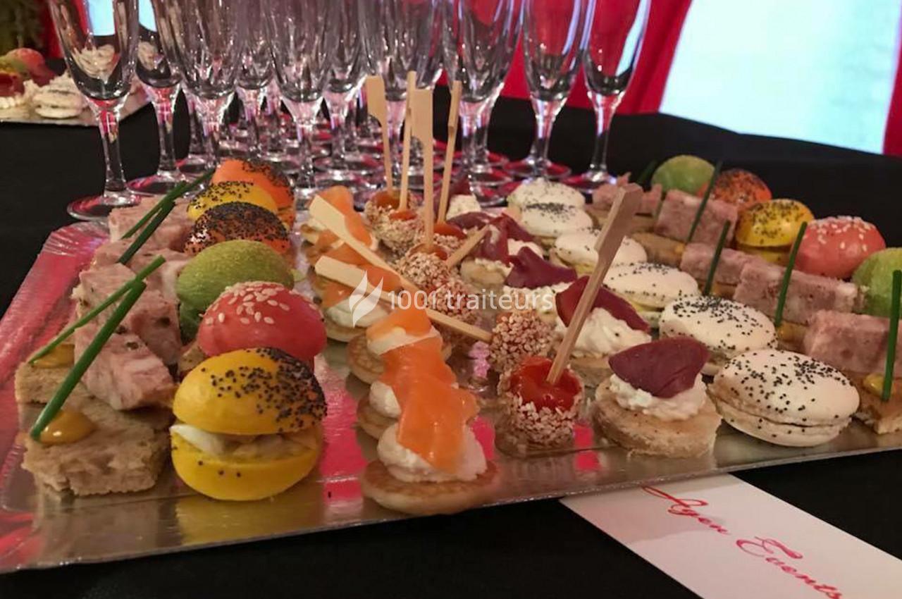 Plateau de bouchées apéritives variées avec verrines en arrière-plan sur une table noire.