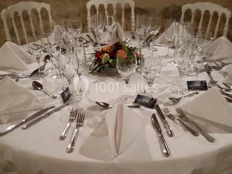 Table dressée avec nappes blanches, couverts, verres, serviettes pliées et centre de table floral coloré.