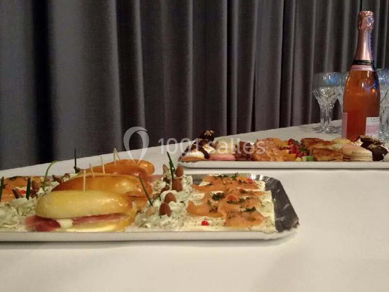 Plateaux de petits fours salés et sucrés avec une bouteille de champagne et des verres sur une table blanche.