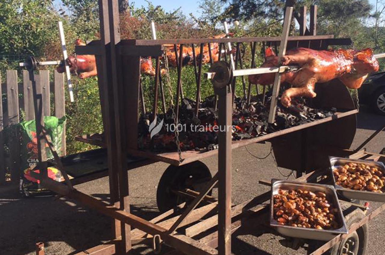 Cochons de lait rôtis à la broche sur un barbecue en plein air, avec des plats de garnitures à proximité.