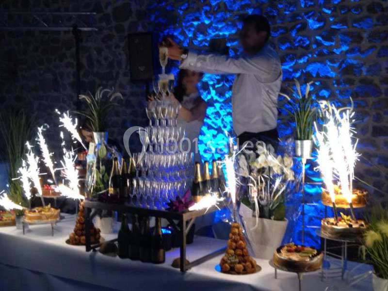 Tour de coupes en verre remplie de champagne, entourée de desserts et de décorations lumineuses dans une ambiance festive.