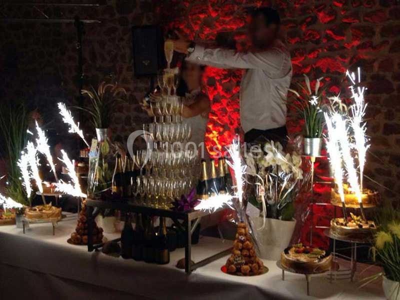 Tour de coupes de champagne illuminée par des feux d'artifice, entourée de desserts et de décorations florales.