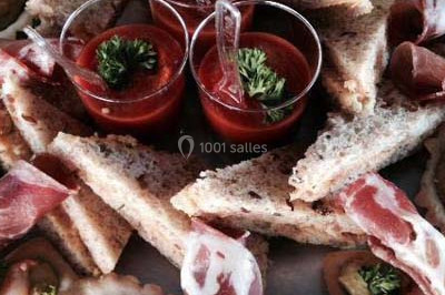 Salle de réception décorée avec des nappes blanches, des tables rondes dressées et un éclairage violet.