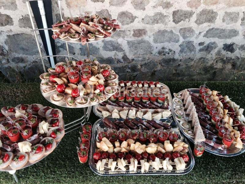 Plateaux garnis de divers amuse-bouches, verrines et canapés disposés sur une table en extérieur.