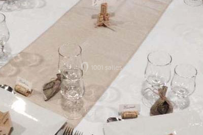 Salle de réception décorée avec des nappes blanches, des tables rondes dressées et un éclairage violet.