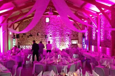 Salle de réception décorée avec des nappes blanches, des tables rondes dressées et un éclairage violet.