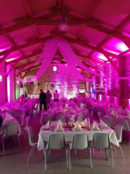 Salle de réception en pierre avec tables dressées et éclairage rose, décorée pour un événement festif.