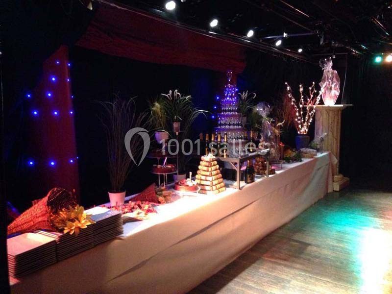 Table de buffet décorée avec des plats variés, une fontaine à champagne et des éléments lumineux dans une salle sombre.