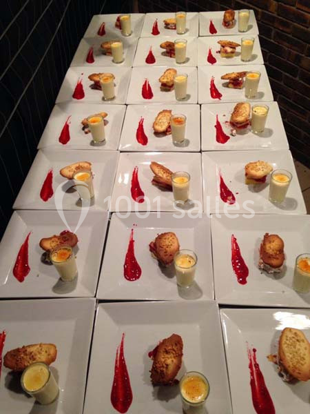 Assiettes dressées avec verrines, toasts et coulis rouge alignées sur une table dans un cadre sombre.