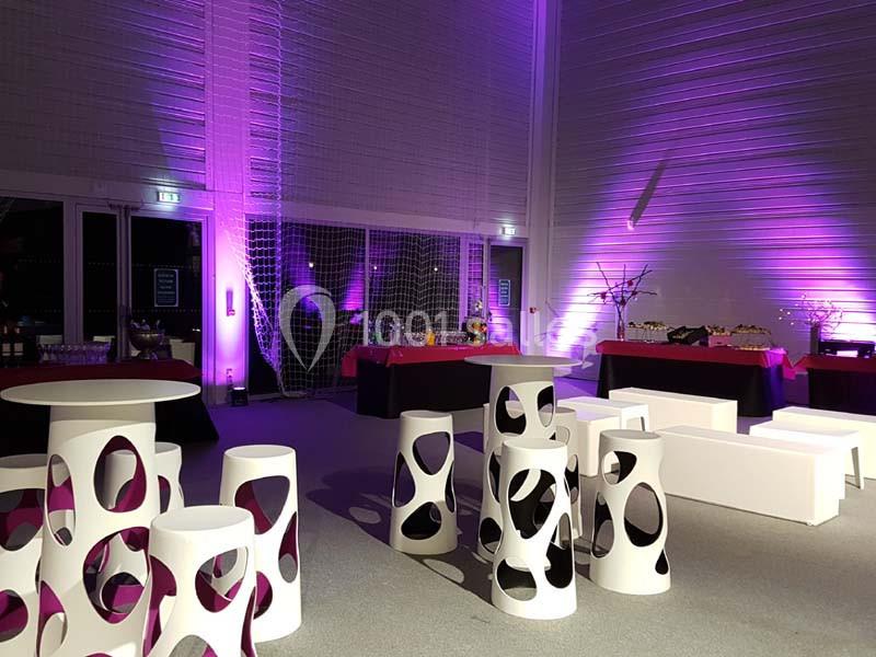 Salle de réception moderne avec éclairage violet, mobilier design blanc et tables de buffet en arrière-plan.