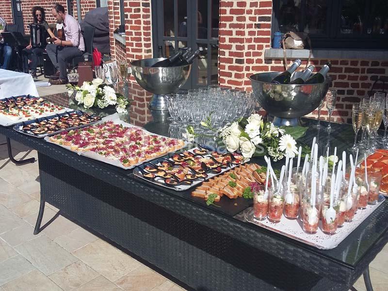 Buffet en extérieur avec verrines, canapés, plats variés et bouteilles de champagne dans des seaux à glace.