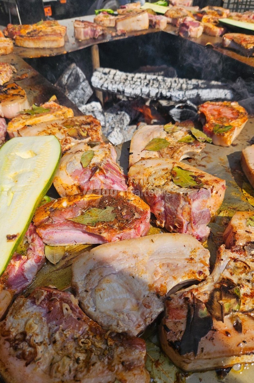 Viandes et légumes grillant sur un barbecue au feu de bois, avec des braises incandescentes en arrière-plan.