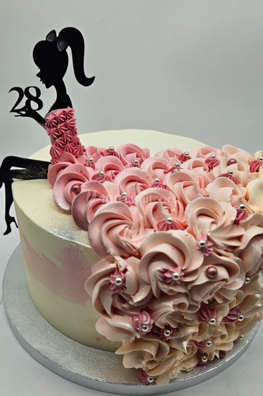 Gâteau décoré de fleurs en crème rose et beige, avec silhouette féminine en chocolat tenant le chiffre 28.