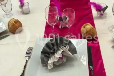 Table dressée pour un mariage avec nappe blanche, chemin de table fuchsia, pliage de serviette et décorations festives.