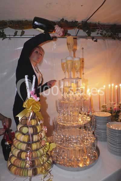 Une femme verse du champagne dans une pyramide de coupes, à côté d'une pièce montée de macarons et de bougies allumées.