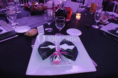 Table dressée pour un mariage avec nappe blanche, chemin de table fuchsia, pliage de serviette et décorations festives.