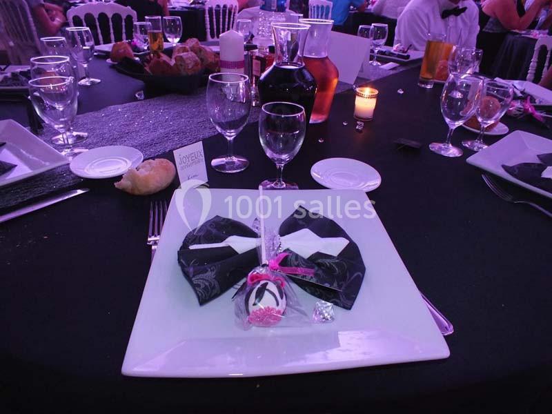 Table dressée avec une assiette carrée, serviette pliée, décoration sucrée et verres sur une nappe noire.