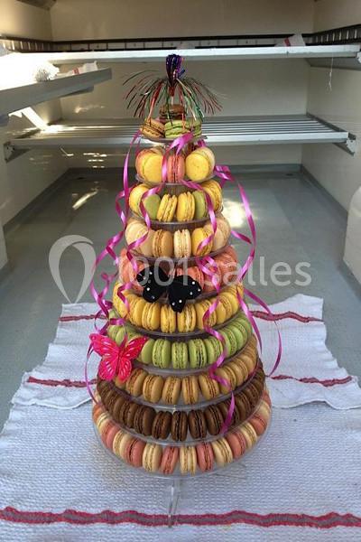Tour de macarons colorés disposés en pyramide, décorée de rubans roses et de papillons en plastique.