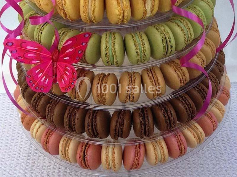 Tour de macarons colorés disposés sur des plateaux transparents, décorée d'un papillon rose et de rubans.