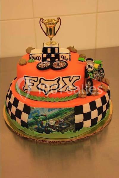 Gâteau décoré sur le thème de la moto-cross avec trophée, moto miniature et motifs de drapeaux à damier.
