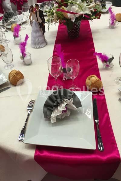 Table dressée pour un mariage avec nappe blanche, chemin de table fuchsia, pliage de serviette et décorations festives.