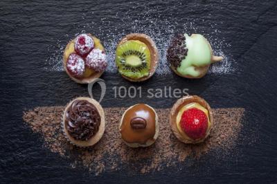 Tour de coupes en verre illuminée et gâteau à étages décoré de fleurs roses sur une table de réception.
