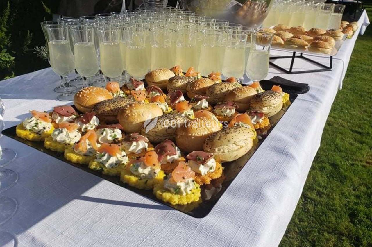 Plateau de mini-sandwichs garnis et verres de boisson claire disposés sur une table blanche en extérieur.