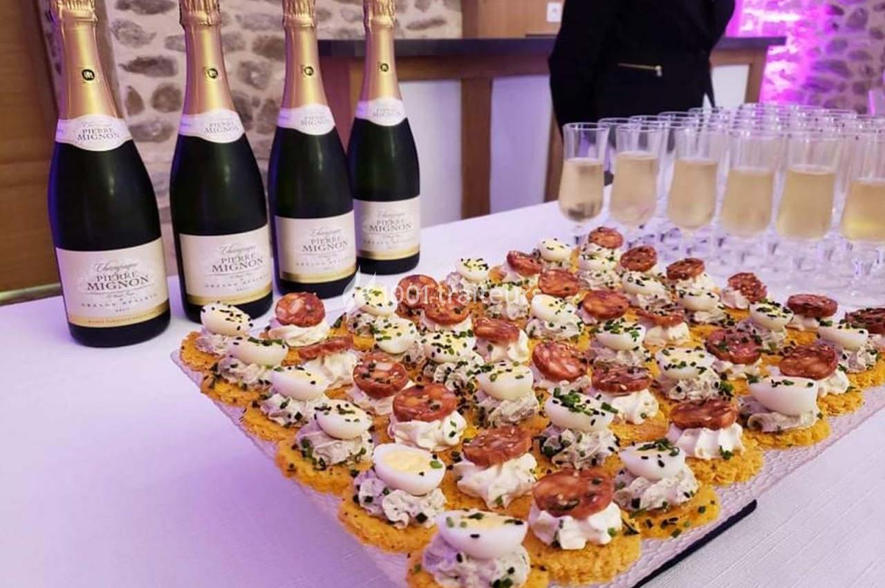 Plateau de bouchées apéritives garnies de crème et de charcuterie, avec des bouteilles de champagne en arrière-plan.