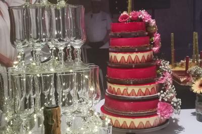 Tour de coupes en verre illuminée et gâteau à étages décoré de fleurs roses sur une table de réception.
