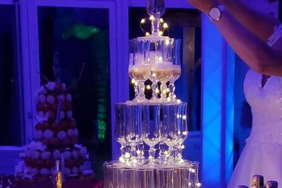 Tour de coupes en verre illuminée et gâteau à étages décoré de fleurs roses sur une table de réception.