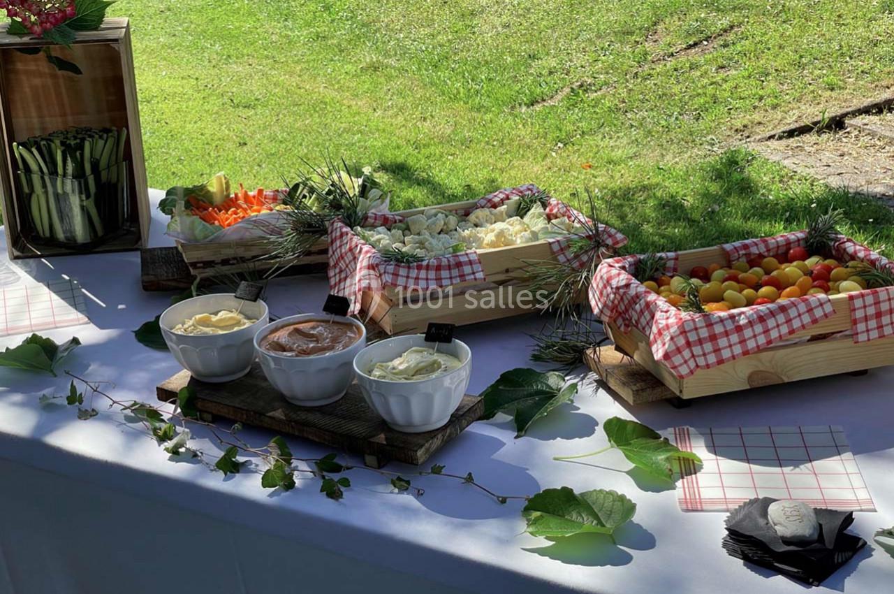 Buffet en plein air avec légumes frais, sauces en bols et décorations naturelles sur une nappe blanche.