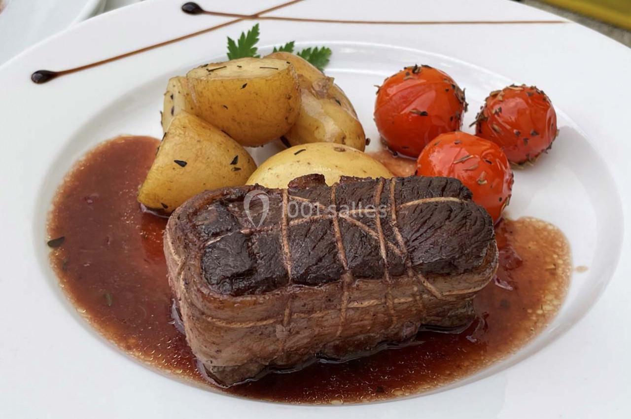 Plat de viande rôtie avec sauce, accompagné de pommes de terre et tomates cerises grillées, servi sur une assiette blanche.