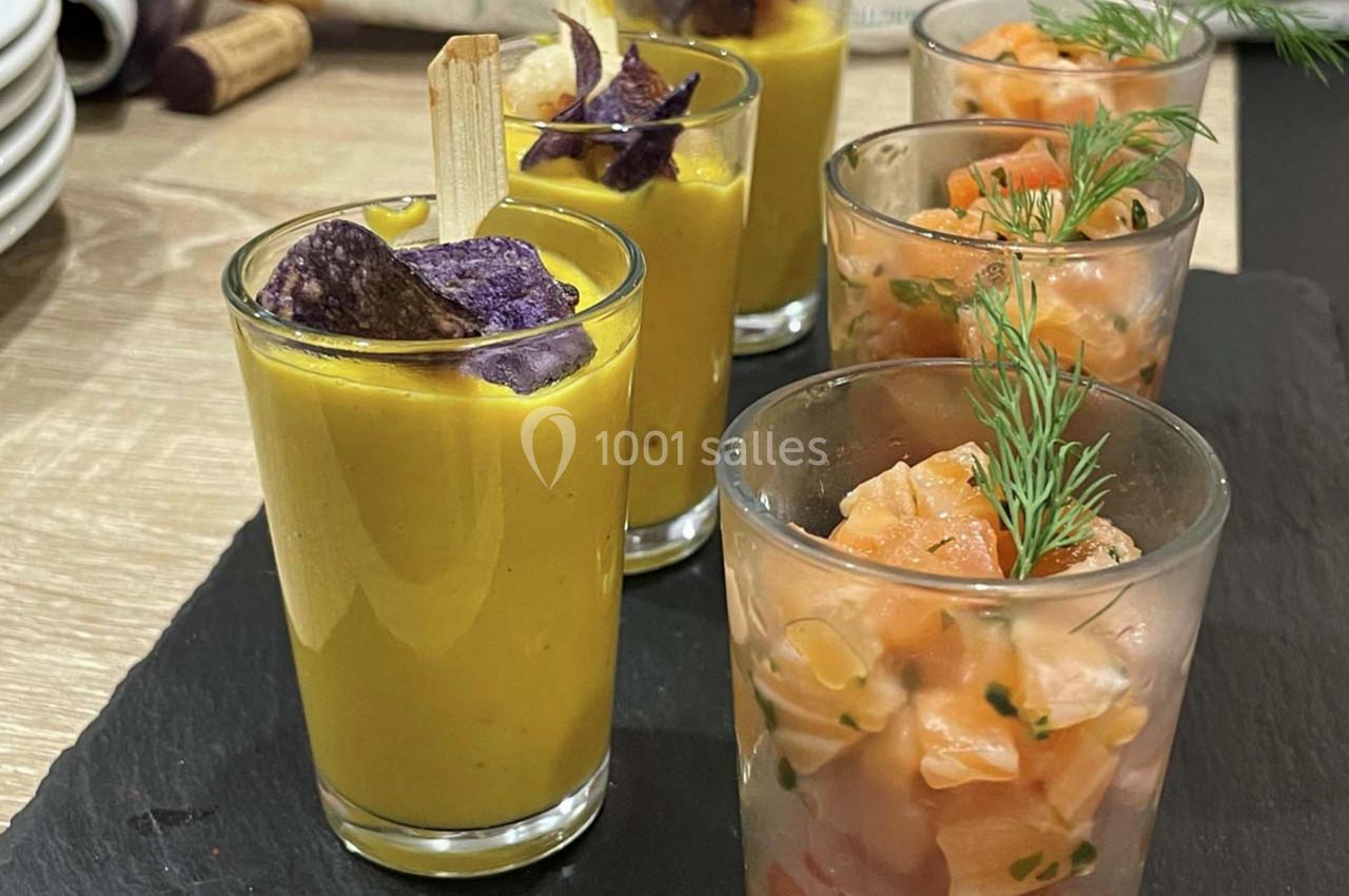 Verrines de soupe jaune garnies de chips violettes et tartares de saumon décorés d'aneth, présentées sur un plateau.