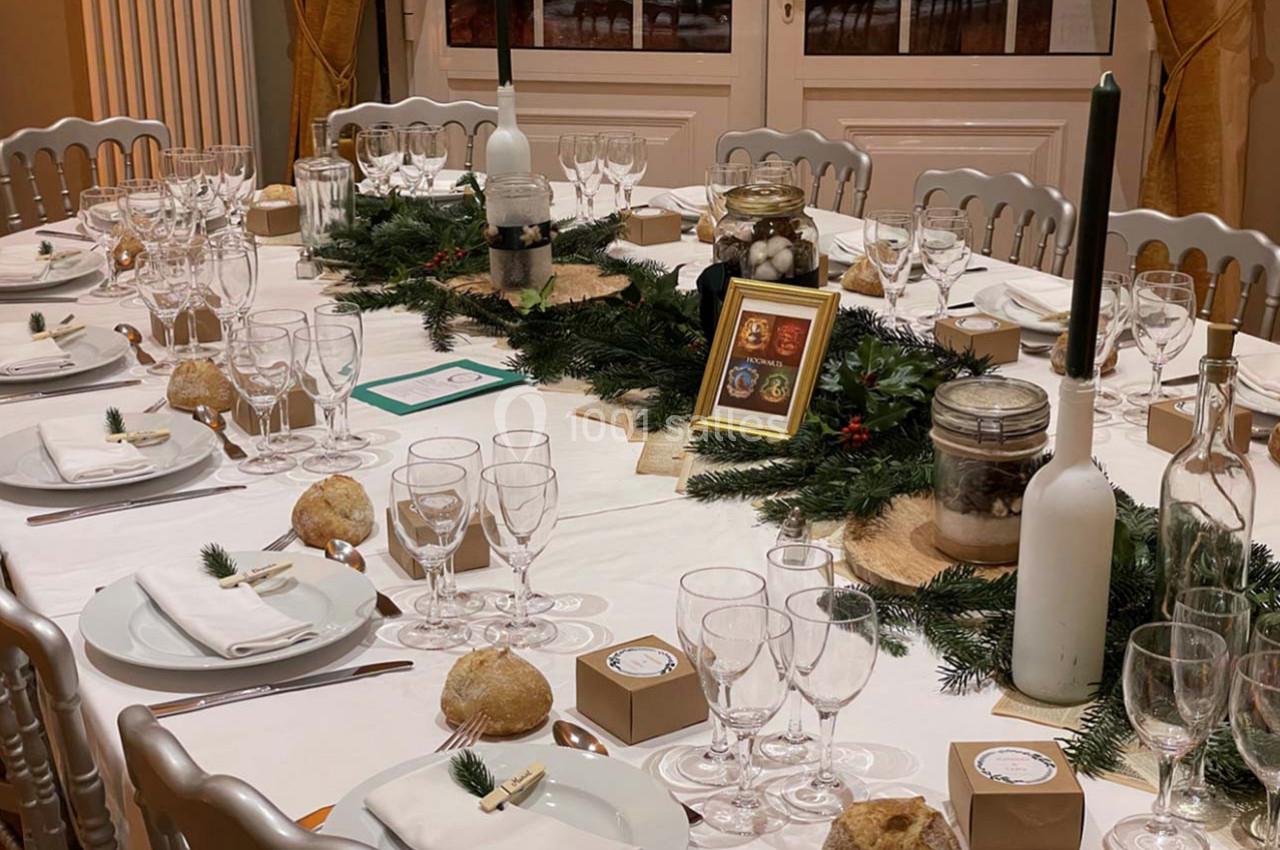 Table décorée pour un repas festif avec nappes blanches, verres, bougies, décorations végétales et petits cadeaux.