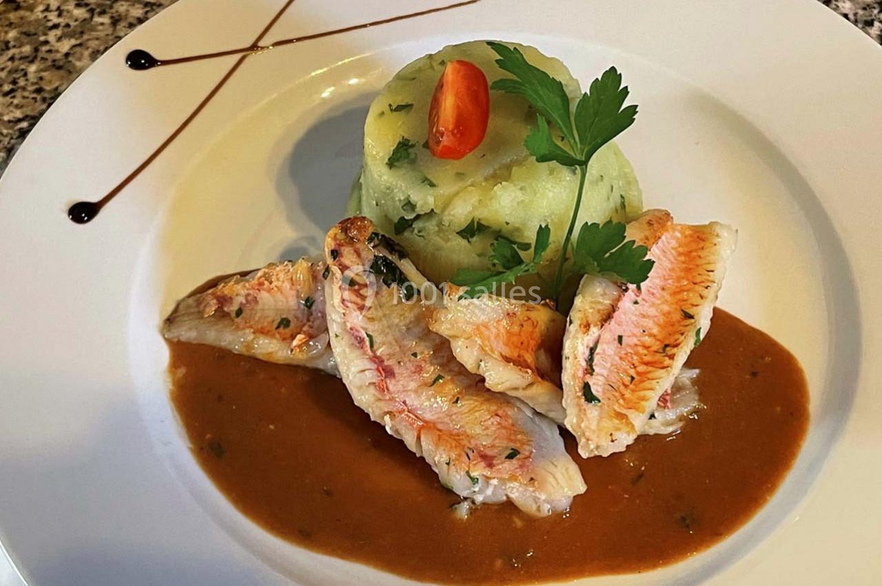 Filets de poisson accompagnés de purée aux herbes, décorés de sauce et d'une tomate cerise sur une assiette blanche.