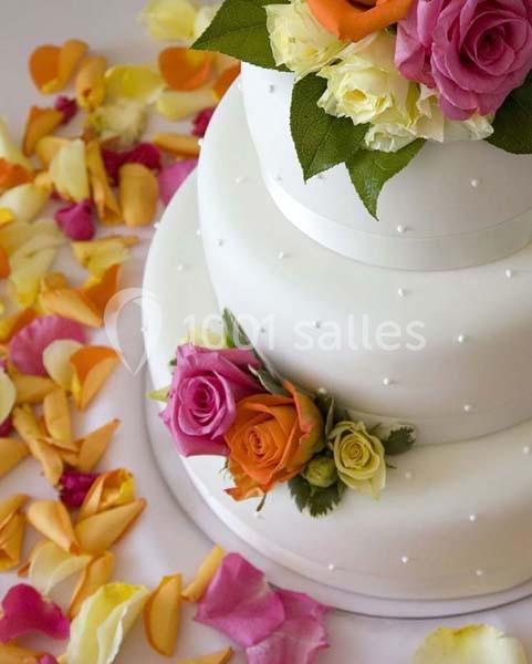 Gâteau de mariage blanc décoré de roses colorées, entouré de pétales de fleurs jaunes, roses et orange.