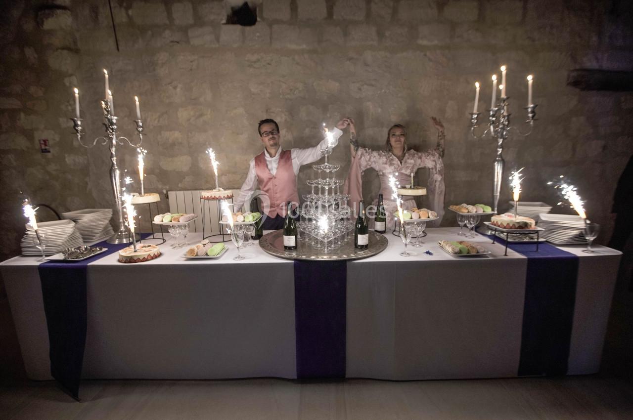 Un couple debout derrière une table de réception décorée, entourée de chandeliers et de desserts, avec une fontaine à…