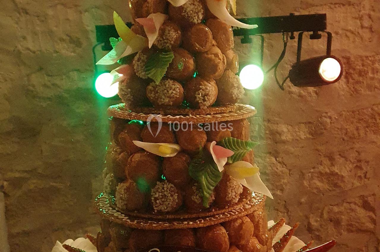 Pièce montée de choux décorée de fleurs en sucre et figurines de mariés, avec une inscription personnalisée.