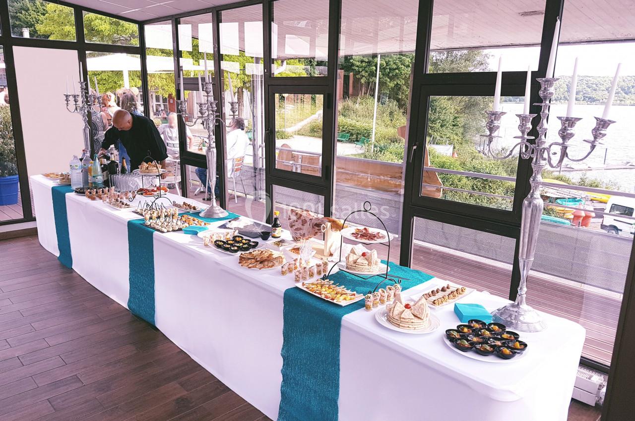 Table de buffet élégamment dressée avec divers plats et desserts, située dans une salle lumineuse avec vue sur l'extérieur.