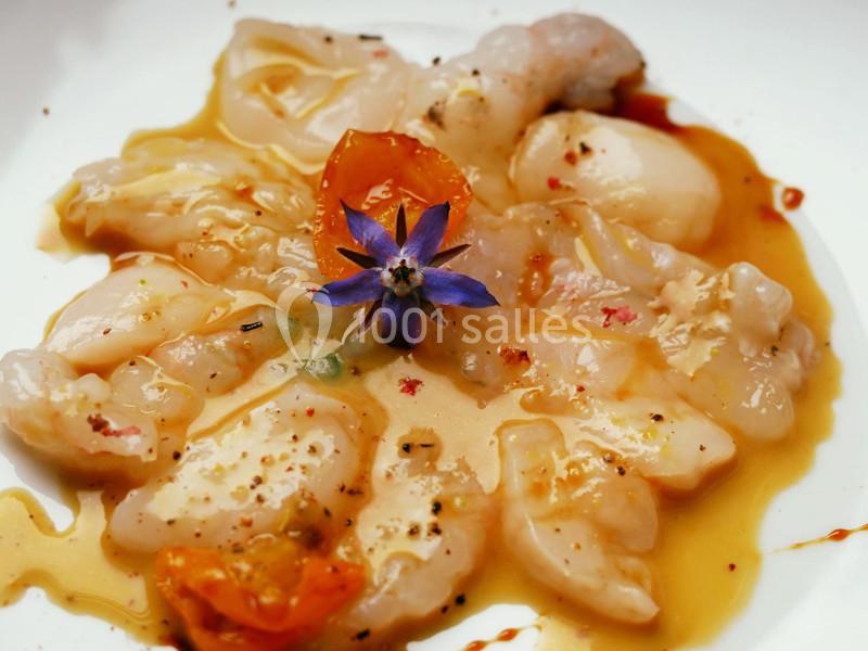 Carpaccio de poisson cru avec une fleur comestible violette, assaisonné d'huile et de poivre, décoré de tomates.