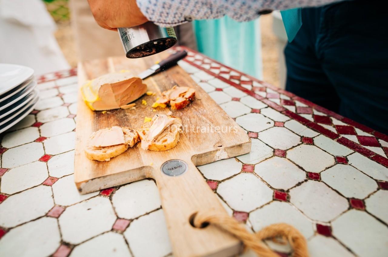 Personne moulant du poivre sur des tranches de foie gras disposées sur une planche en bois.